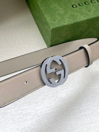 Beige leather belt close-up with round silver-tone GG buckle and stitching detail