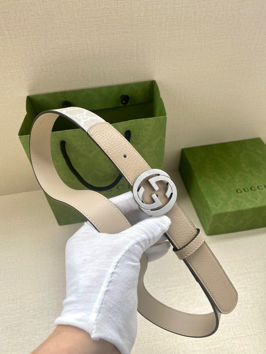Gucci belt with light beige leather strap and silver GG buckle, shown on hand