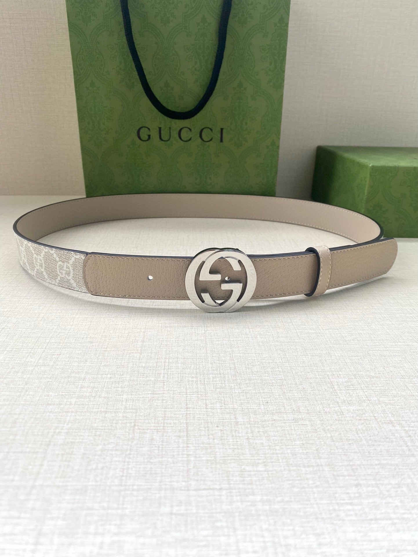 Beige leather belt laid flat with circular silver-tone GG buckle centered