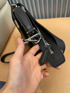 Black leather-look crossbody bag with zipper track, metal rings, and logo patch