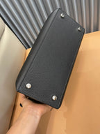 Black leather handbag with textured finish, top handle, and small stud feet