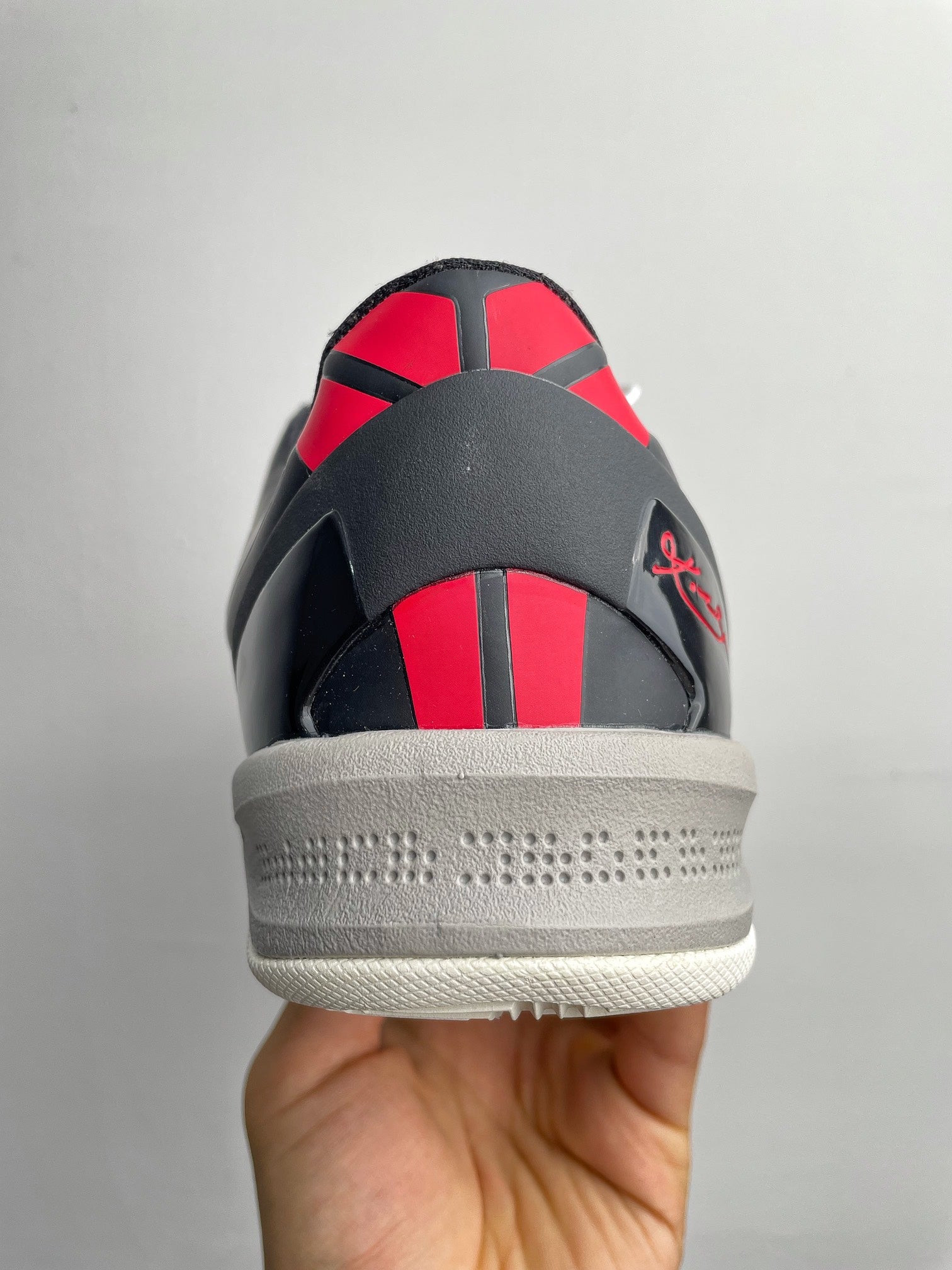 Basketball sneaker heel view with black and red striped back, textured gray sole.
