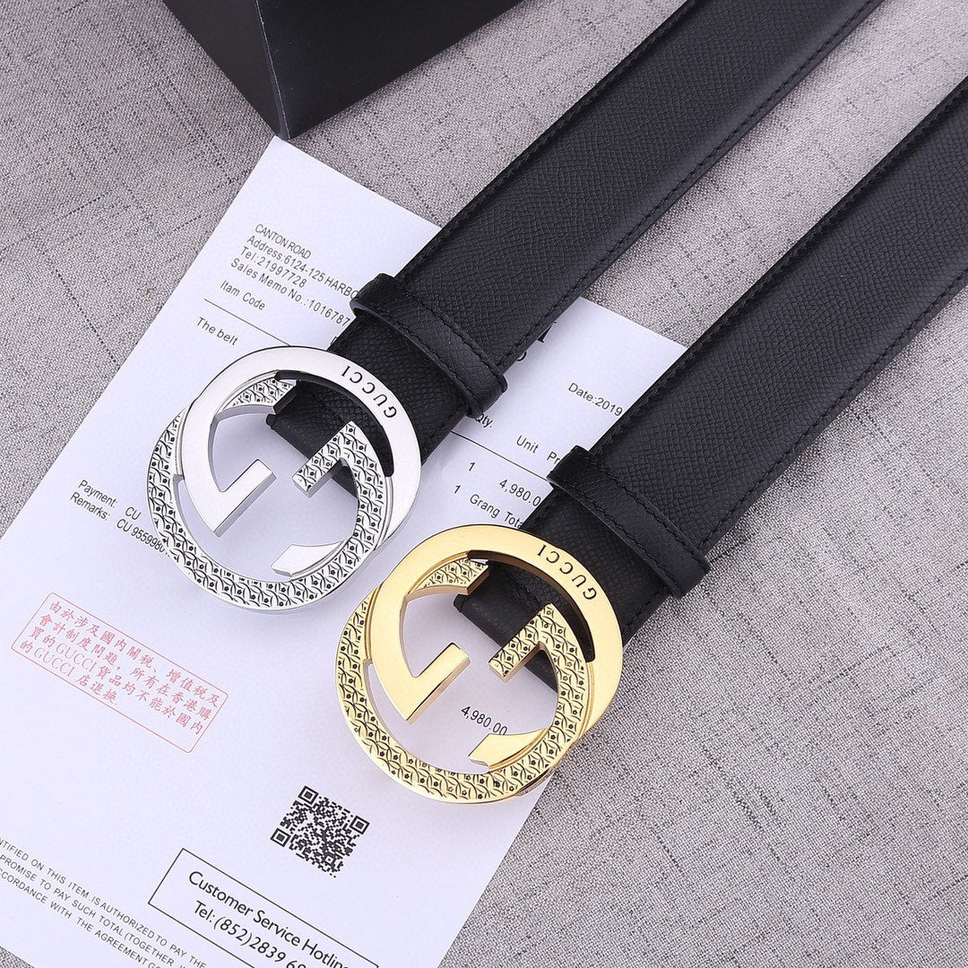 Two black leather Gucci belts with silver and gold-toned GG buckles on papers