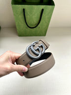 Leather belt detail: taupe strap with gray interlocking GG buckle; hole row visible
