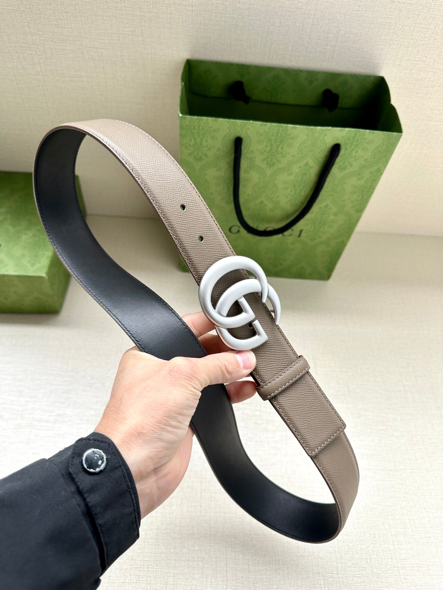 Two-tone leather belt showing white-toned interlocking GG buckle; light strap and dark lining