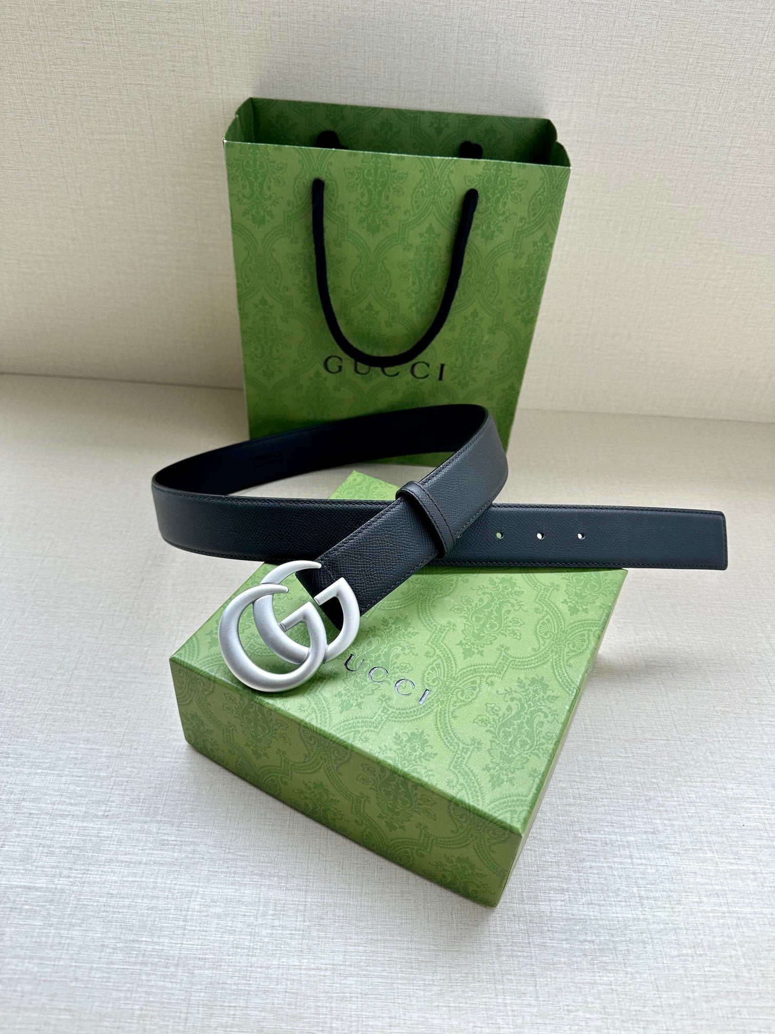 Navy leather belt with silver GG buckle, strap positioned across flat surface.