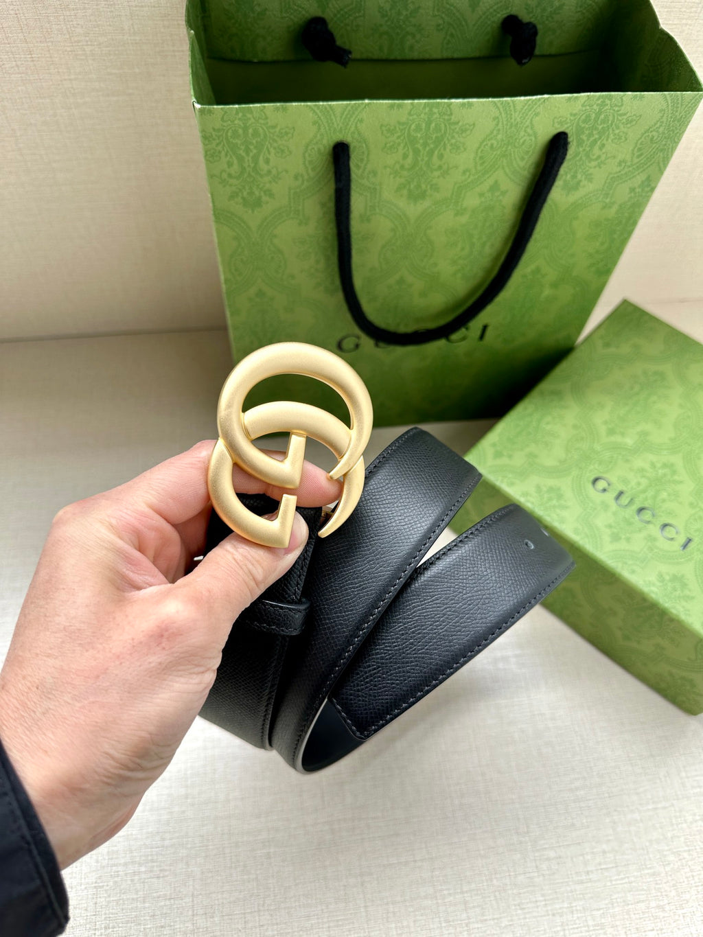 Navy leather belt with gold GG buckle, strap held up showing ring detail.