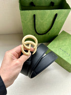 Navy leather belt with gold GG buckle, strap held up showing ring detail.
