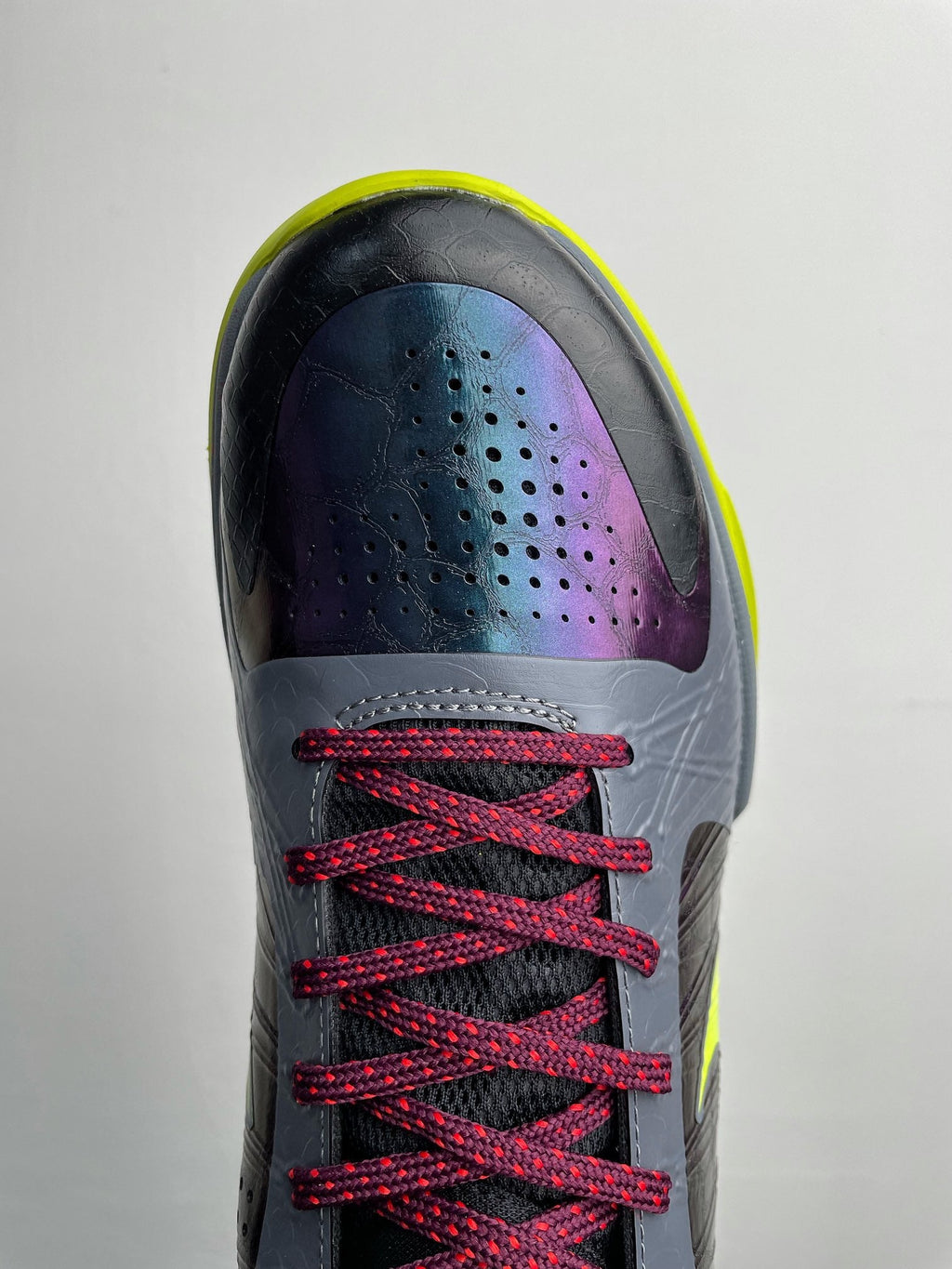 Basketball shoe front close-up: perforated toe, purple fade panel, red laces, neon yellow trim