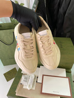 Cream Gucci sneakers shown paired, with lace-up front and brand detailing