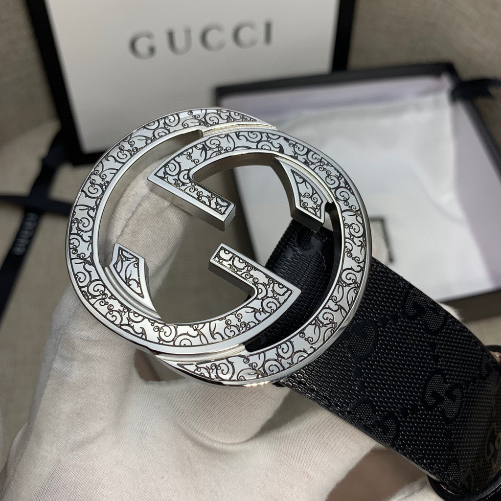Belt buckle close-up on dark GG canvas strap with silver double-G emblem.