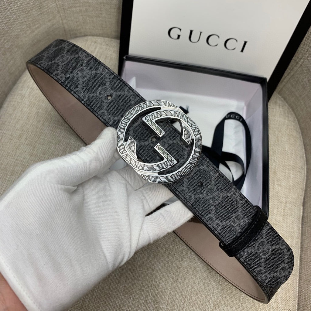 Gucci belt with dark monogram strap and silver G buckle, held in hand.