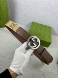 Brown leather belt with round silver G buckle, held in white-gloved hand
