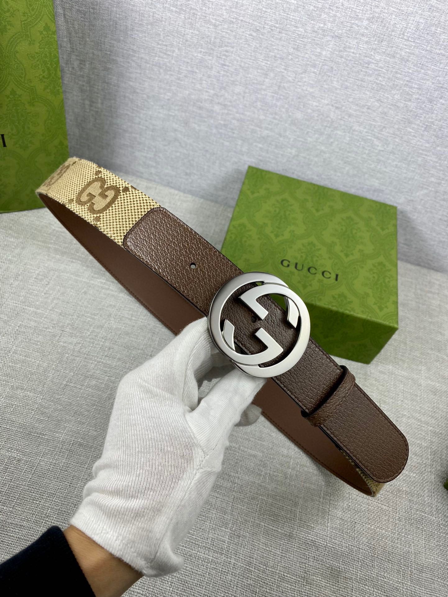 Brown leather belt with round silver G buckle, held in white-gloved hand