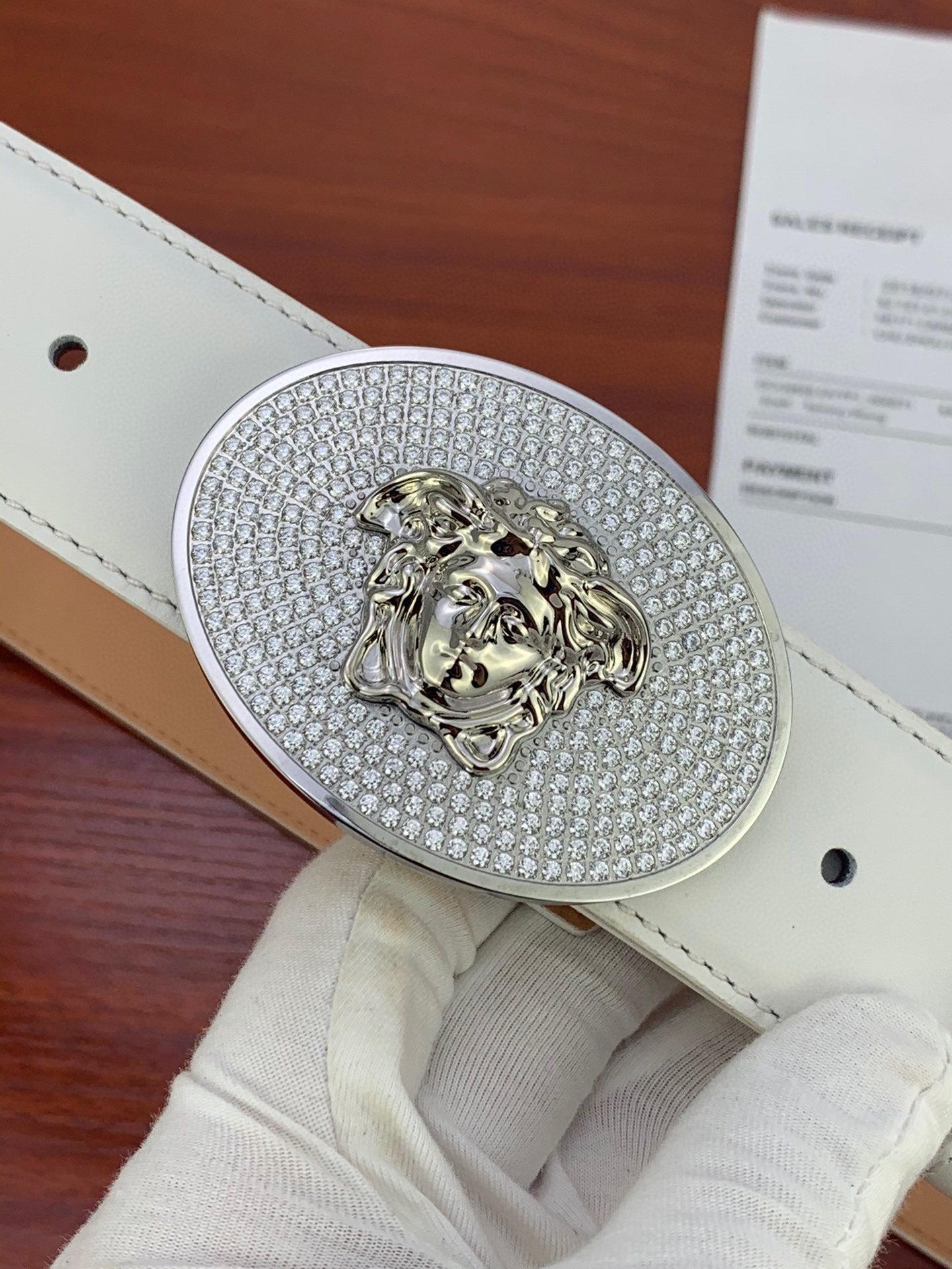 Close-up of oval rhinestone lion buckle on white leather belt