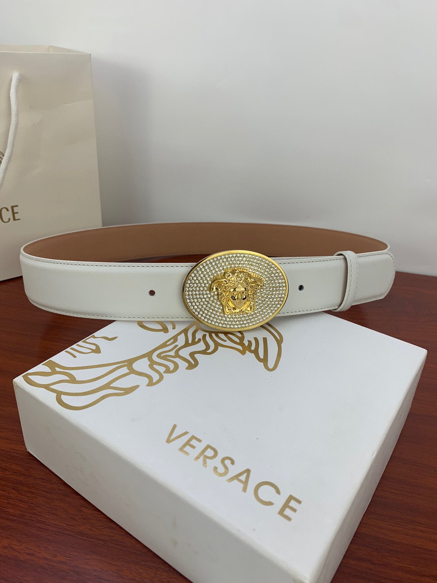 White leather belt with gold oval medallion buckle on Versace gift box
