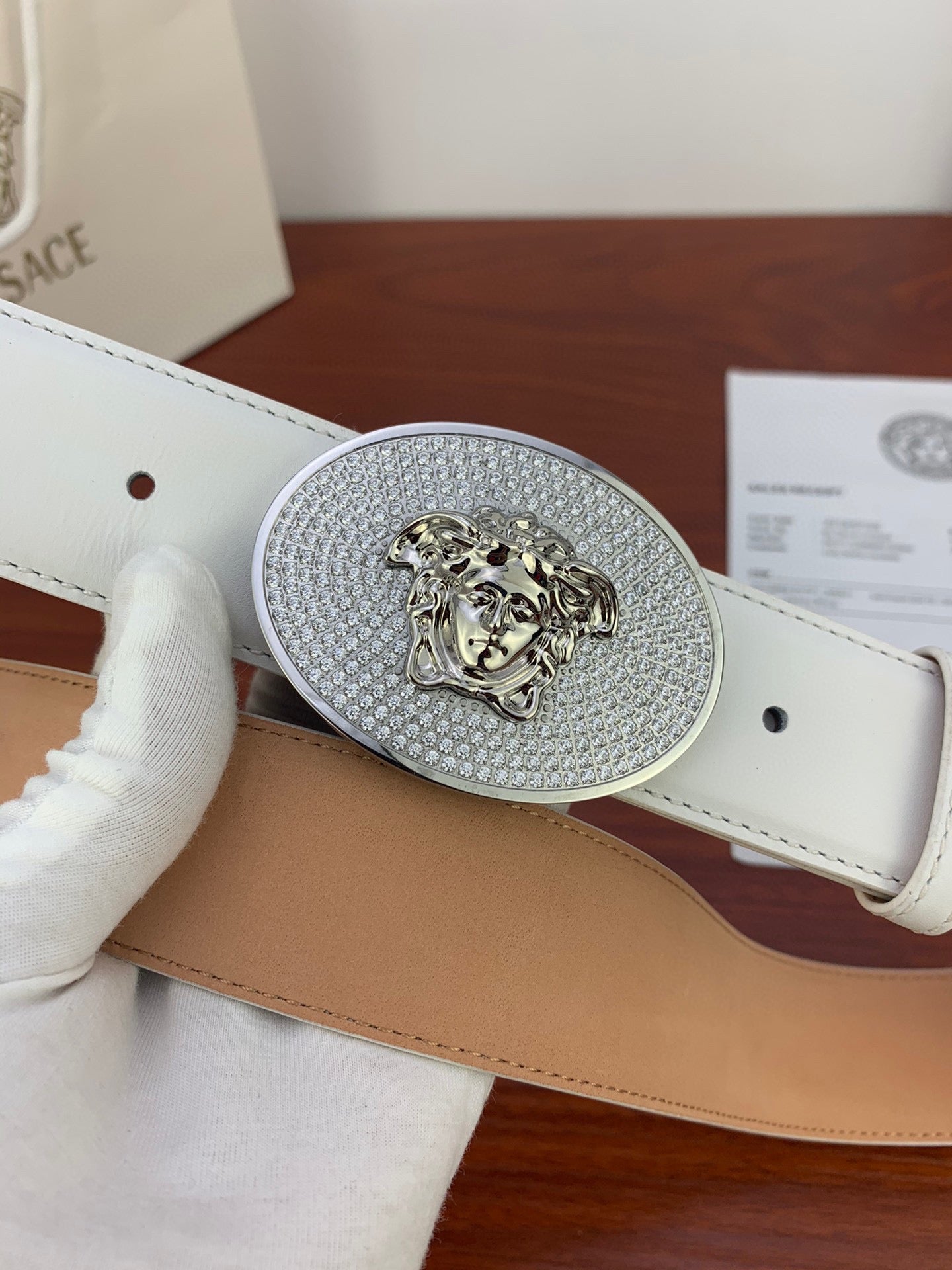 Oval rhinestone lion buckle centered on white leather belt with perforations