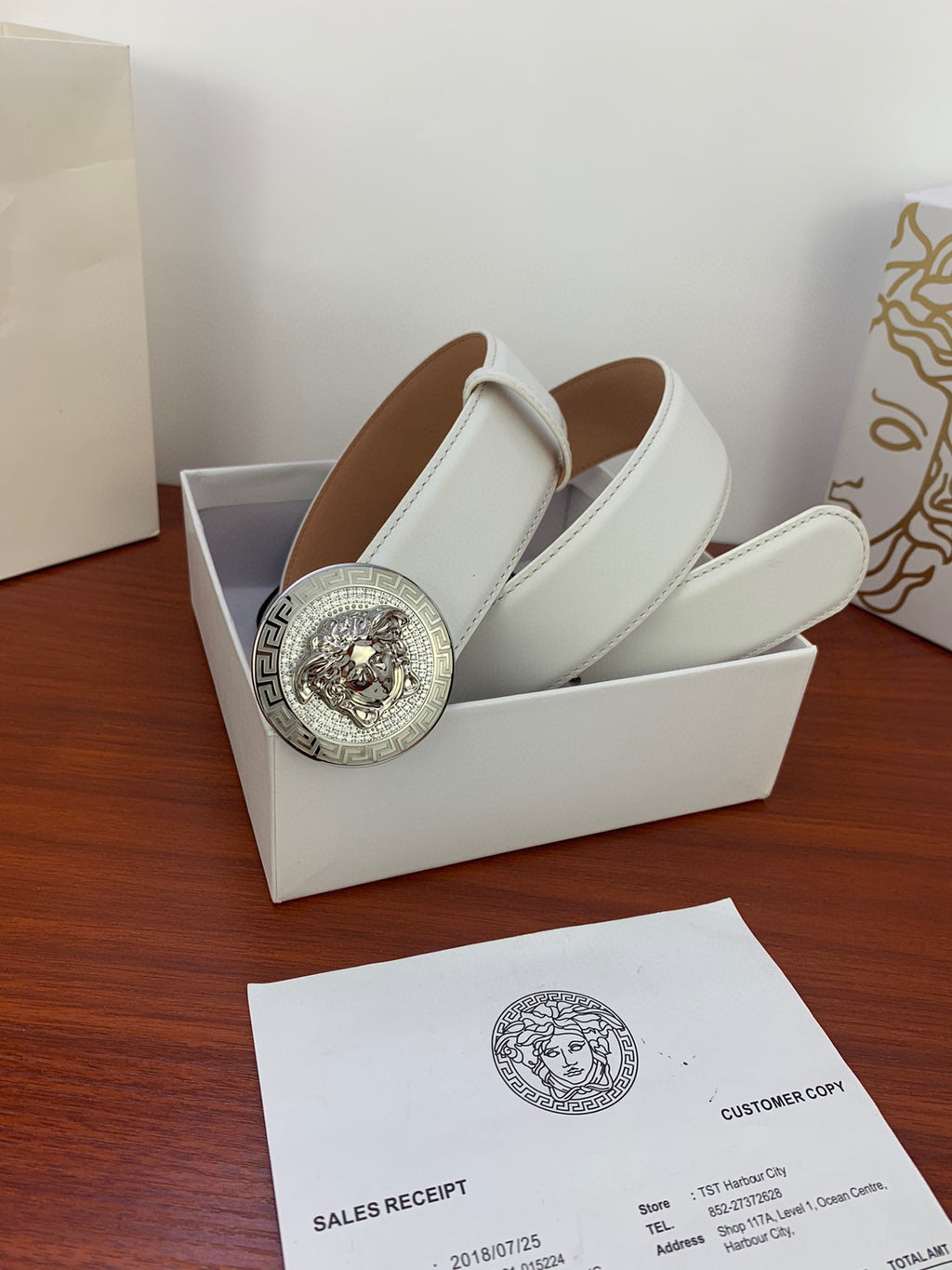White leather belt with silver Medusa medallion buckle, displayed with gift packaging