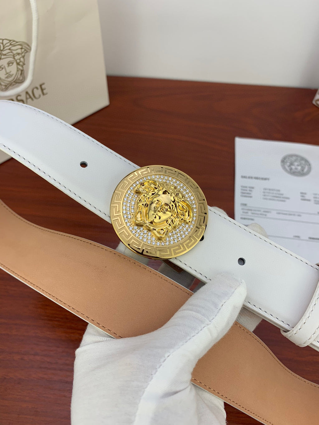 White leather belt with gold circular Medusa buckle, stitched edges and eyelet holes