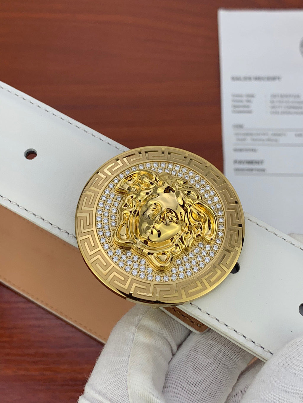 White leather belt close-up with gold Medusa medallion buckle and stitched strap