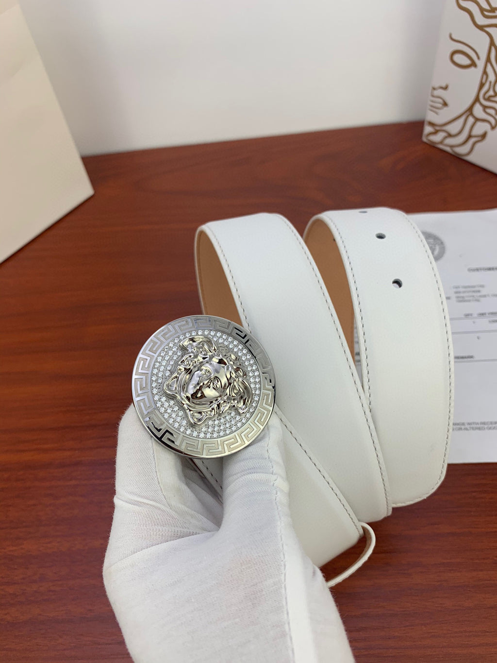 White leather belt with silver Medusa medallion buckle, shown rolled with strap loops