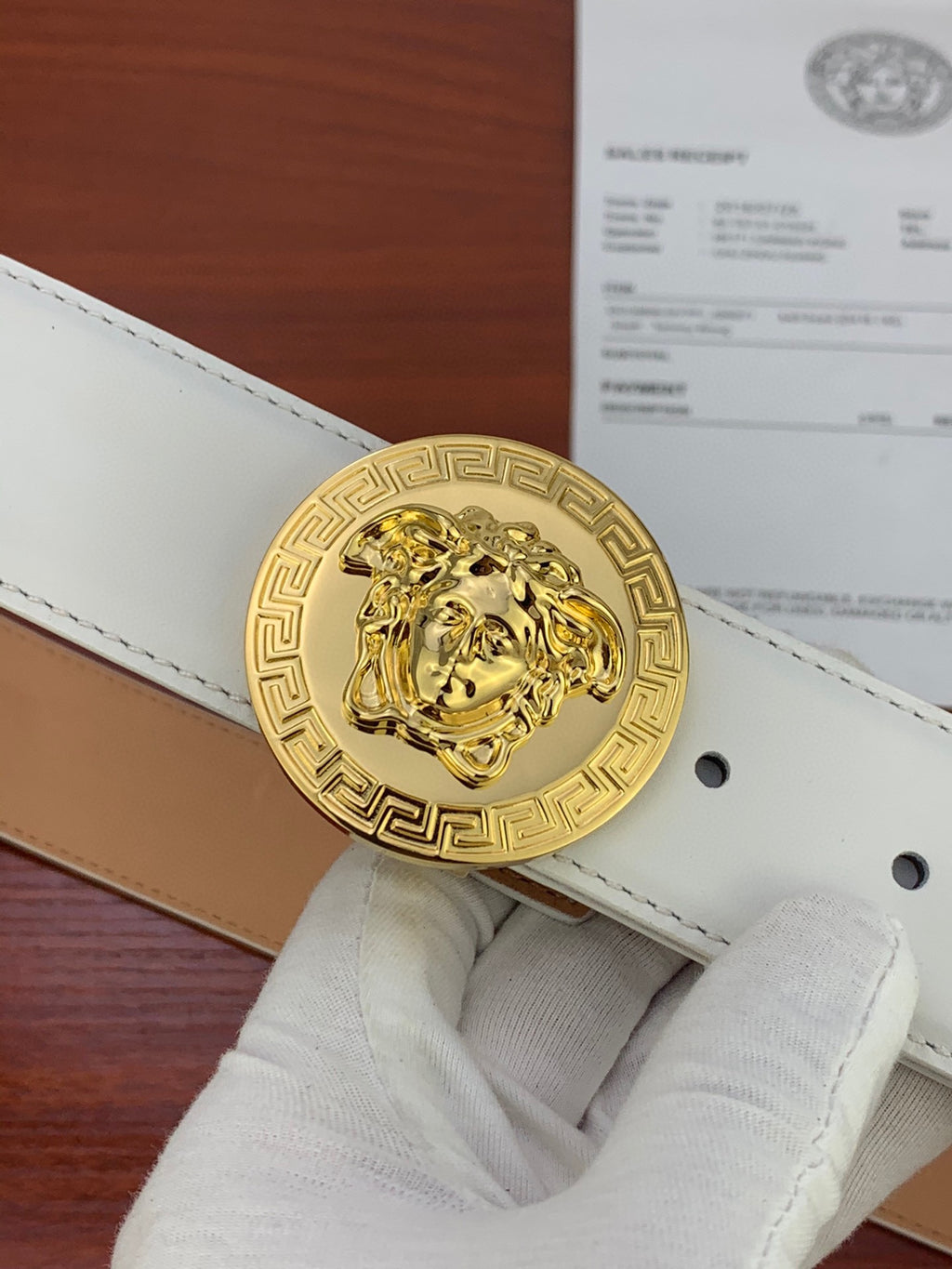 White leather belt with gold round Medusa coin buckle and visible punched holes