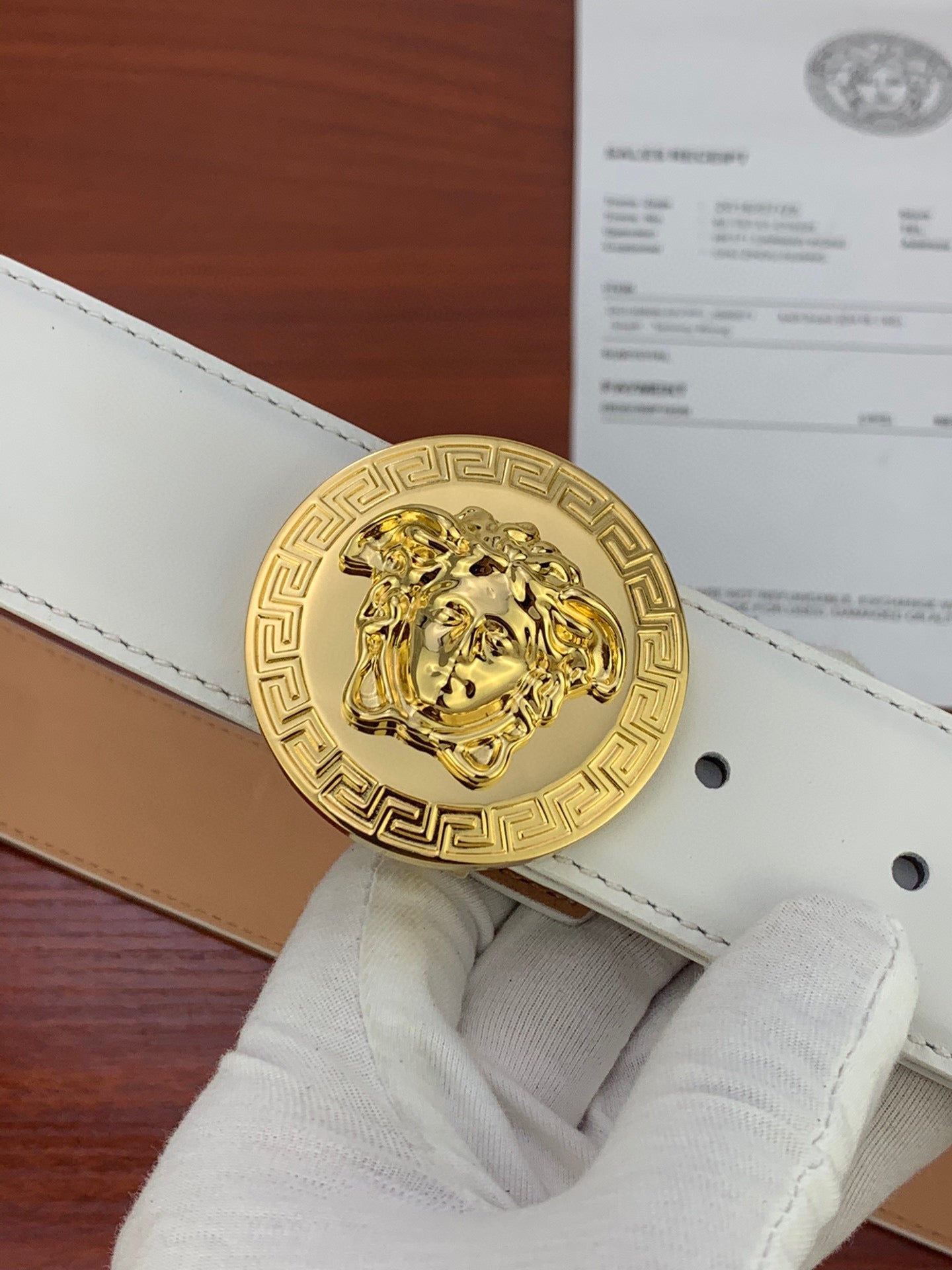 White leather belt with gold round Medusa coin buckle and visible punched holes