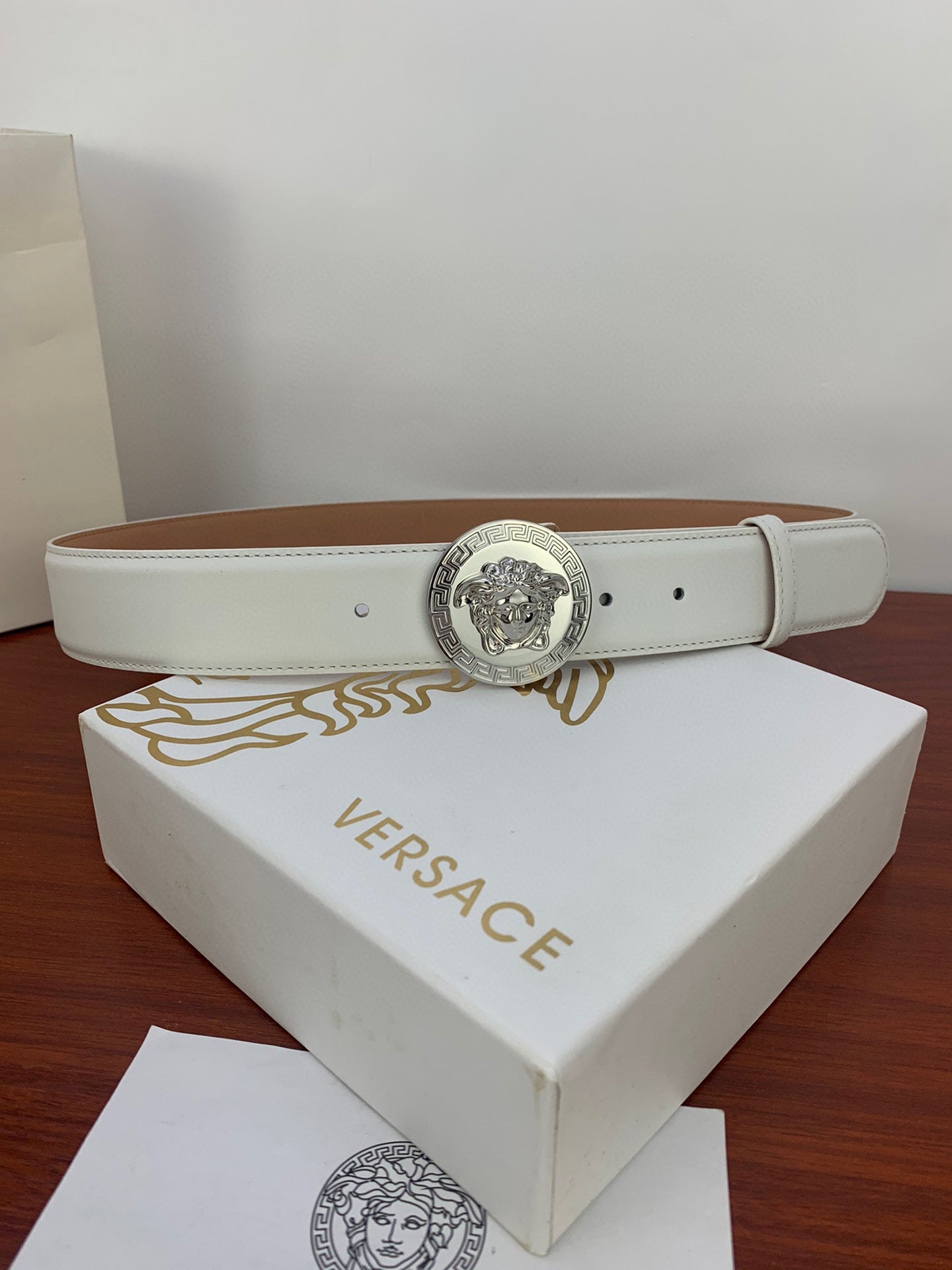 White leather belt with silver Medusa coin buckle, stitched edge, and prong holes