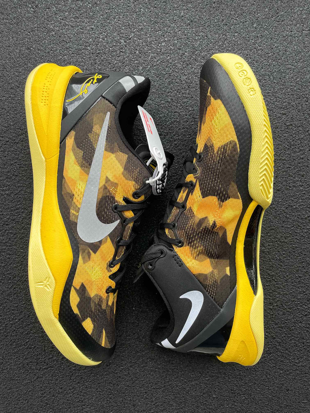 Pair of black and yellow camo basketball shoes with white swooshes