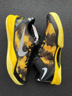 Pair of black and yellow camo basketball shoes with white swooshes