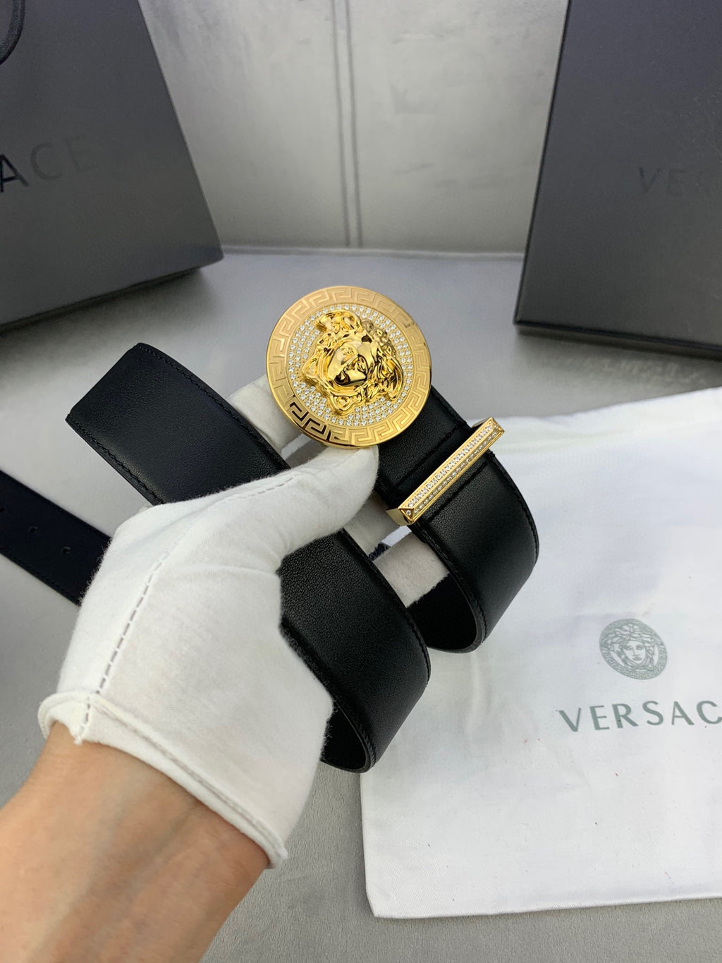 Versace black leather belt with gold medallion buckle held with white glove