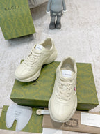 White lace-up sneakers with bunny logo, shown with both shoes on green boxes
