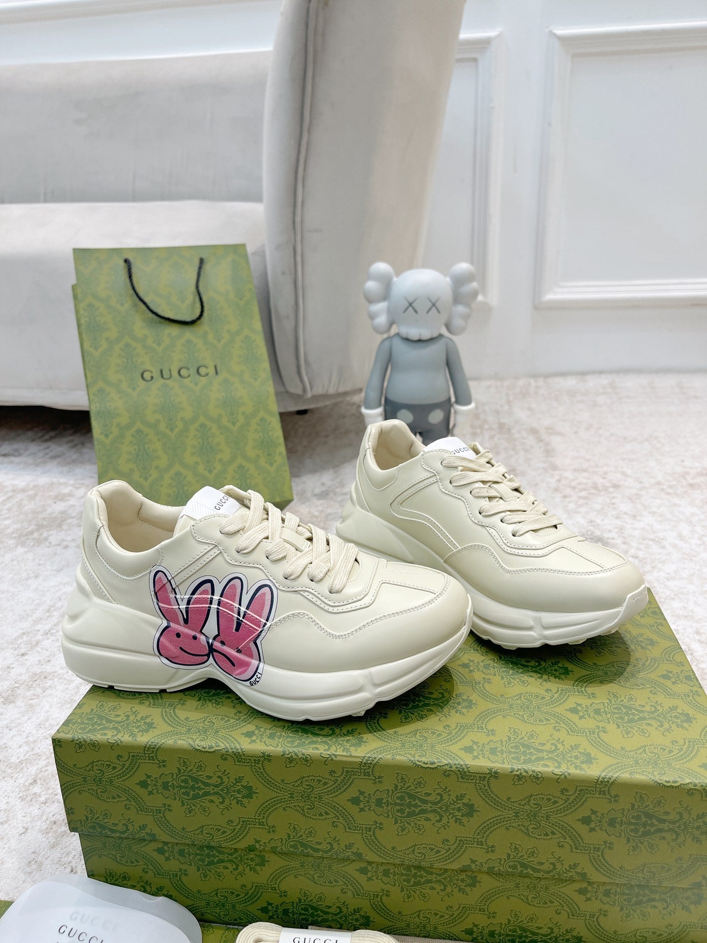 White lace-up sneakers with bunny logo, displayed as a pair on green box