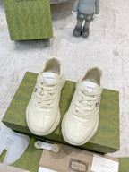 Pair of white Gucci lace-up sneakers with colorful side graphic, front view on boxes
