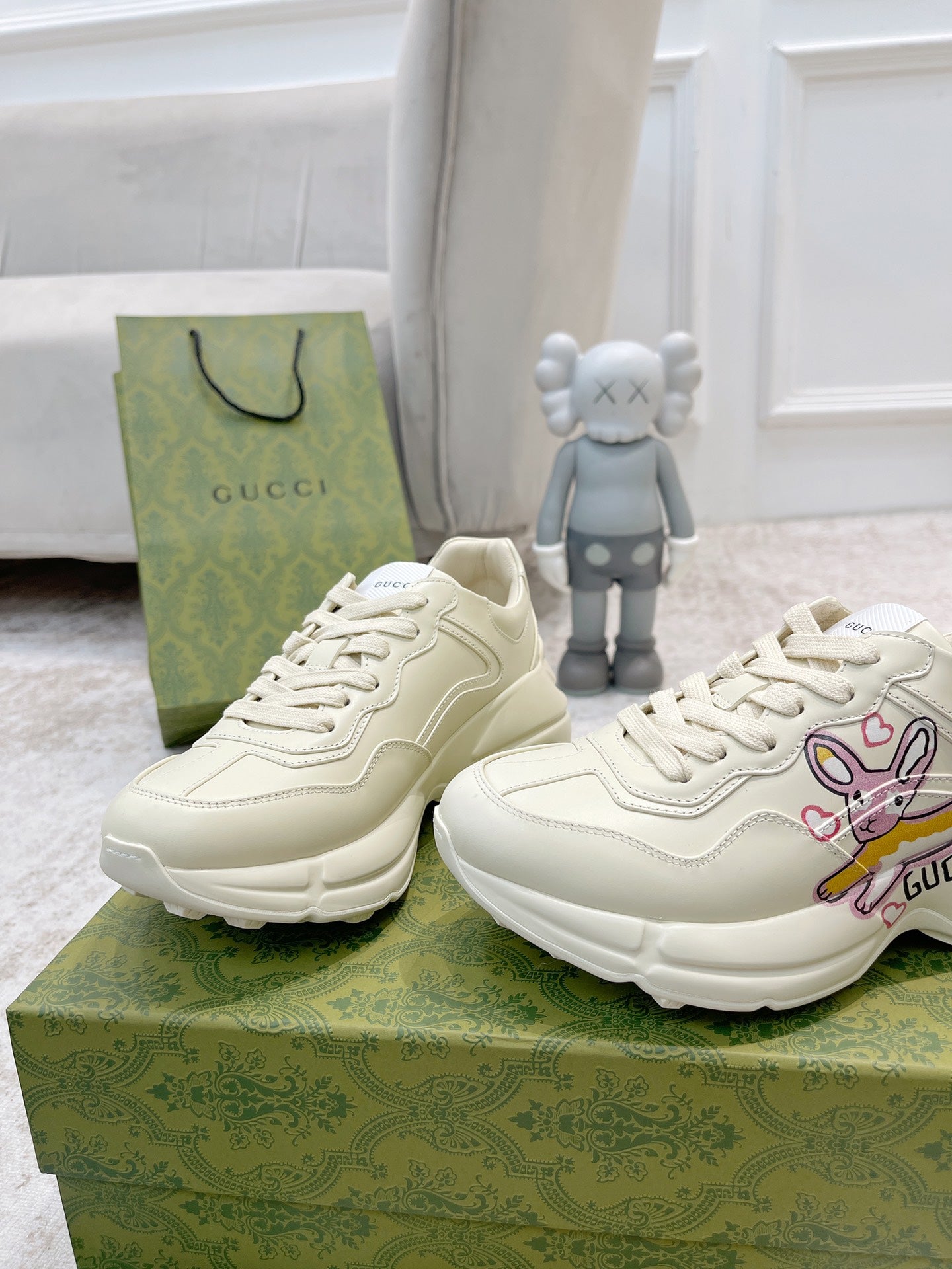 Two white Gucci lace-up sneakers facing forward on green box, side profile visible