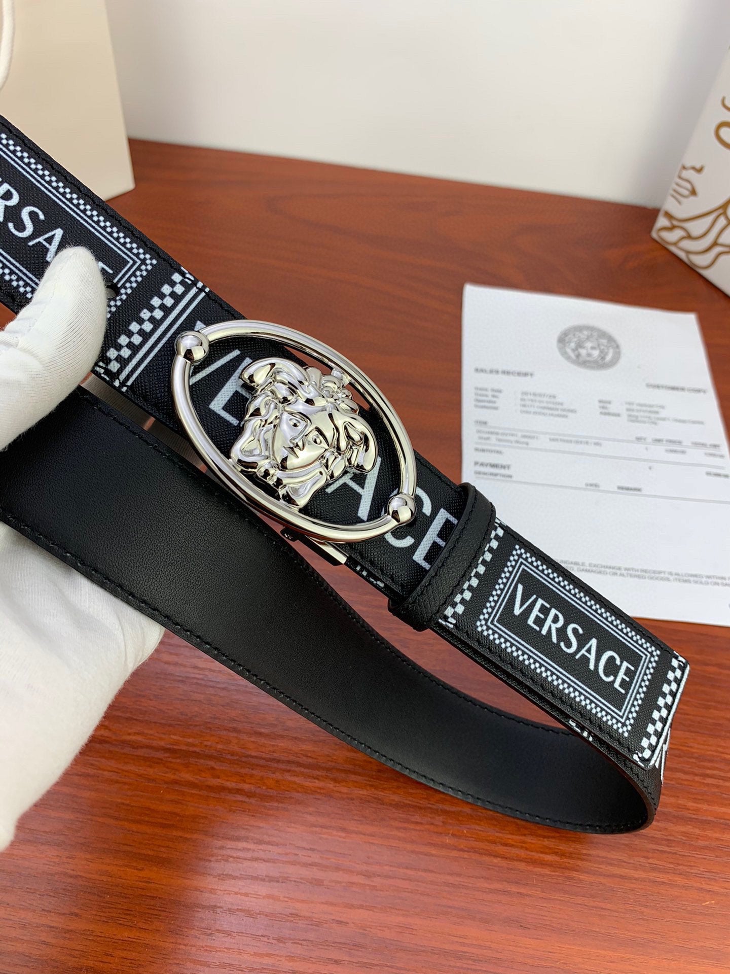 Versace belt close-up: black strap with patterned VERSACE text and silver buckle