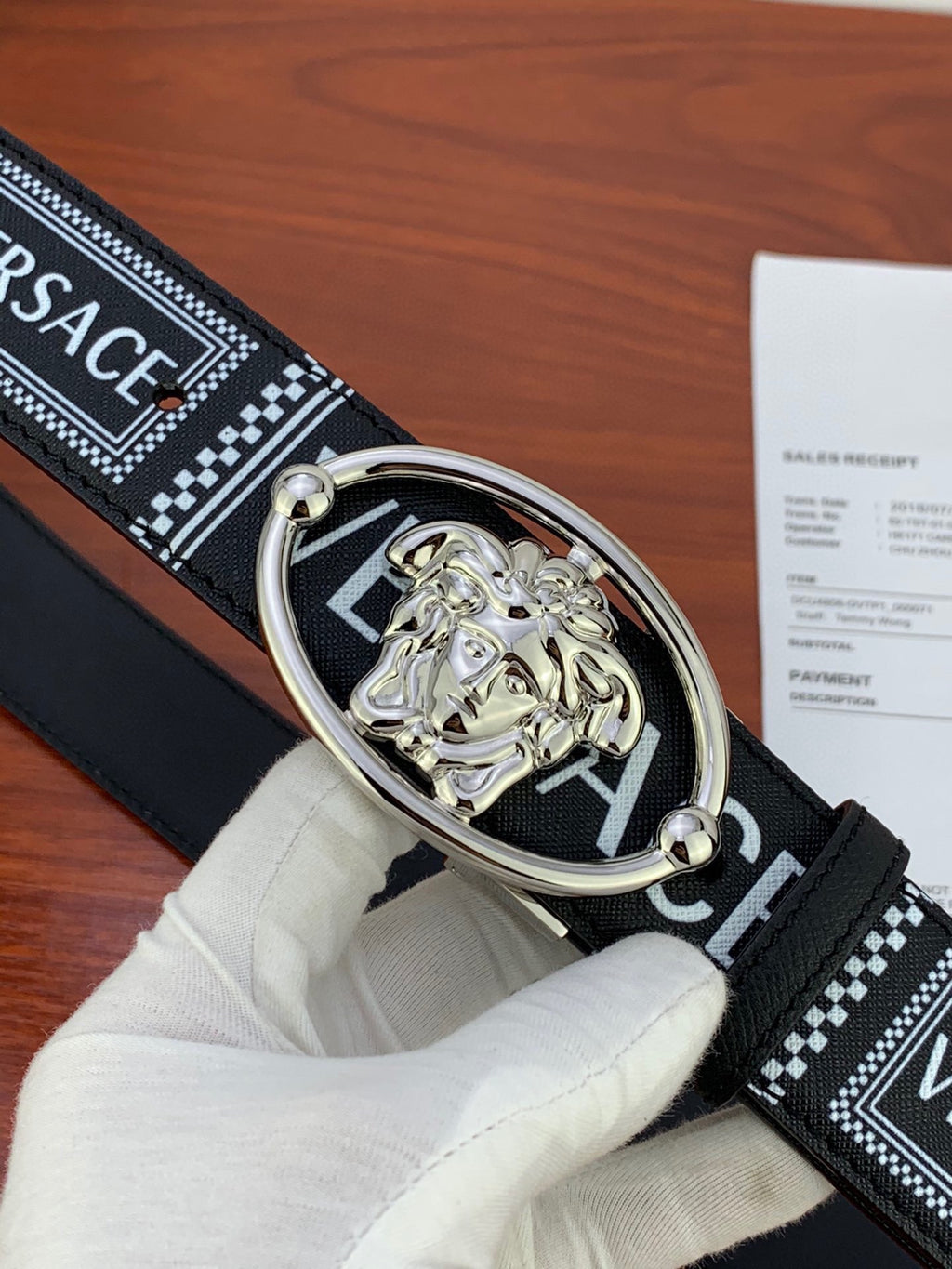Versace belt close-up: black patterned strap with silver oval buckle and lion emblem