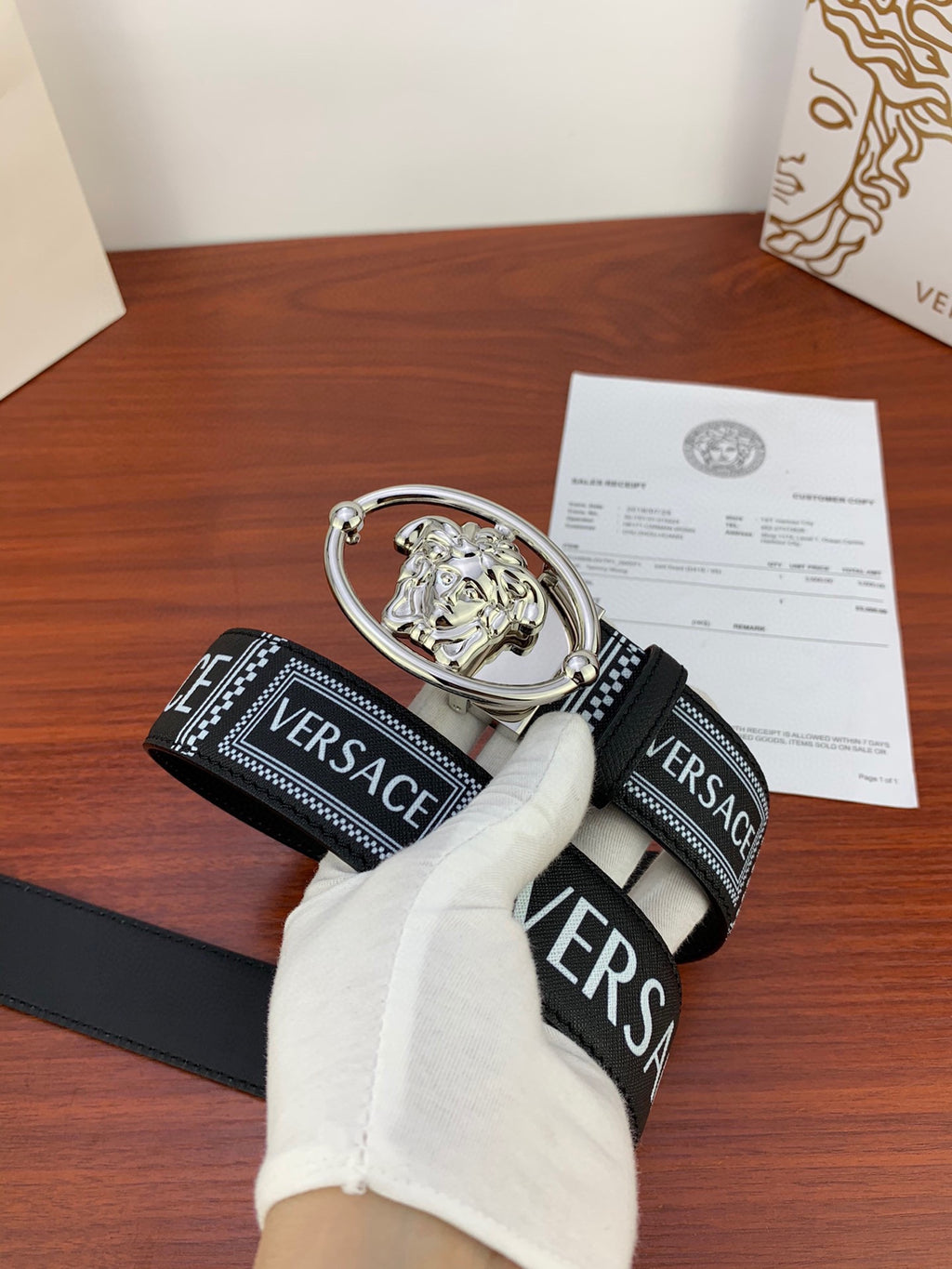 Versace belt with black logo strap and silver oval buckle, partially shown