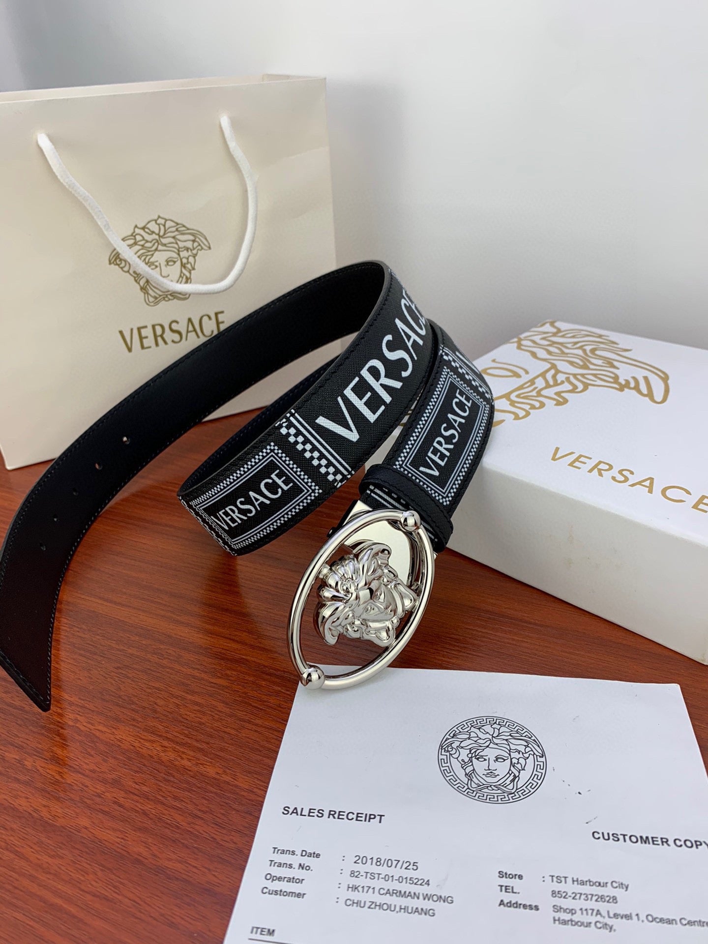 Versace belt resting on packaging: black strap with silver oval buckle