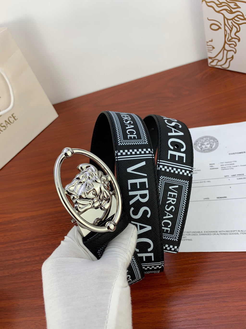Versace belt featuring black logo strap and silver oval buckle with relief emblem