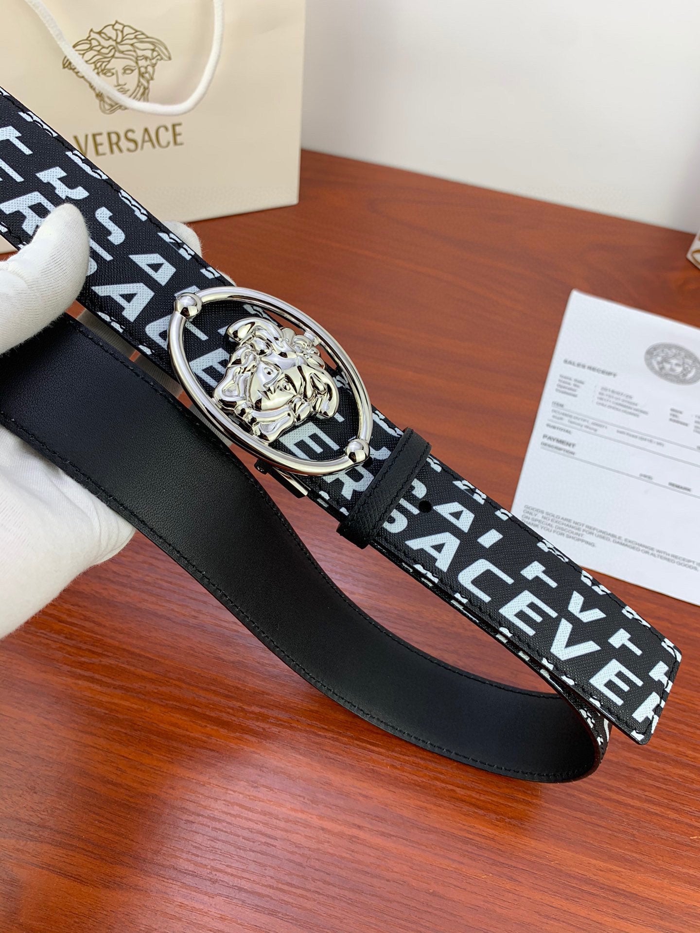 Black Versace belt strap with repeating white logo and silver Medusa oval buckle, close-up