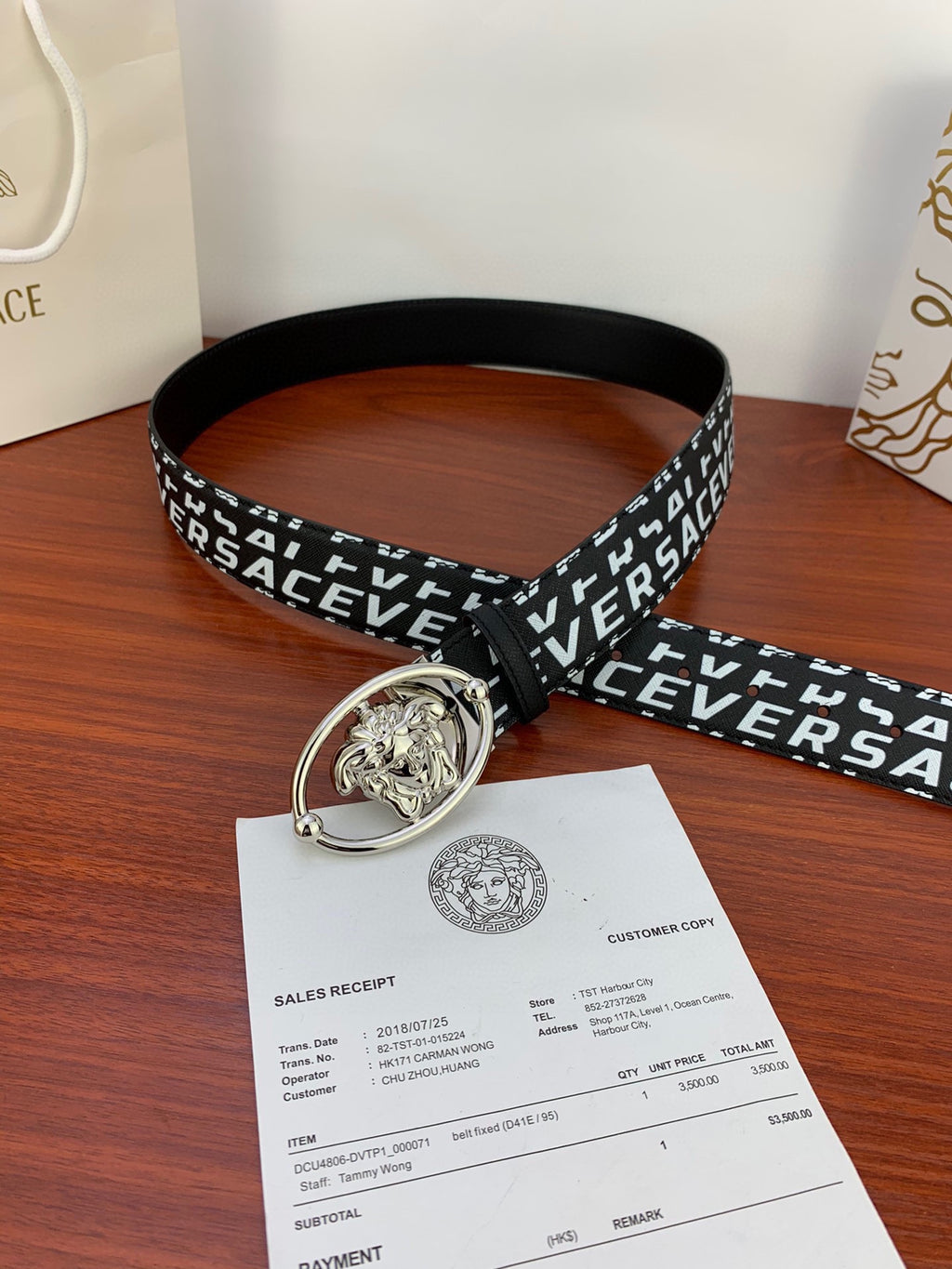 Black Versace belt with repeating white logo and silver Medusa oval buckle, angled