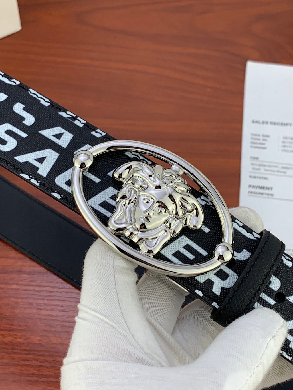 Silver Medusa oval buckle on black Versace belt with repeating white logo
