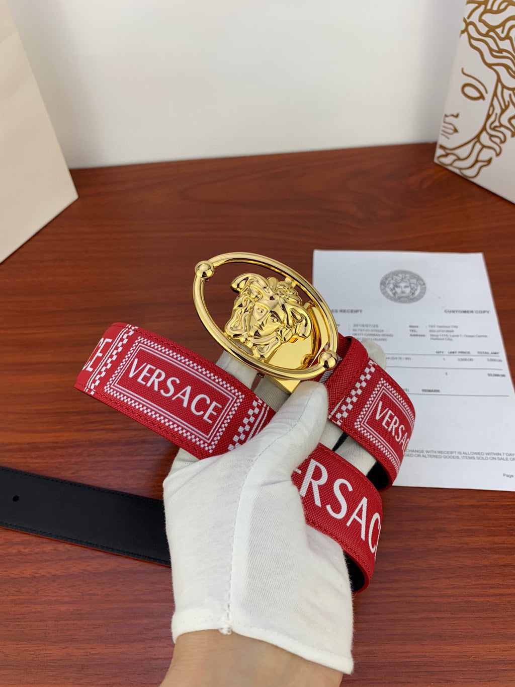 Versace belt end with gold Medusa buckle and red strap, branded VERSACE trim on both sides.