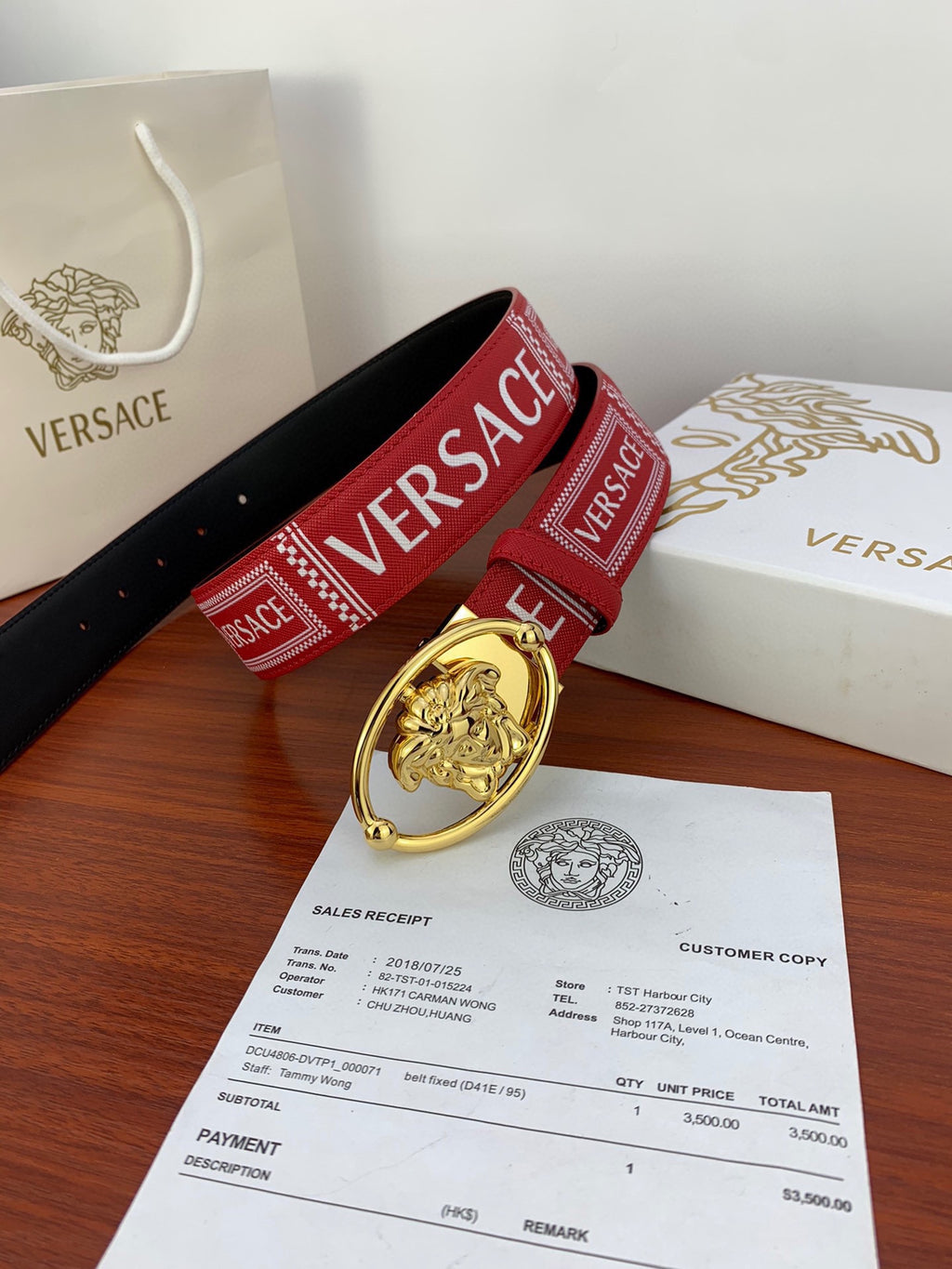 Versace belt with red logo strap and gold Medusa buckle laid across white packaging and receipt.
