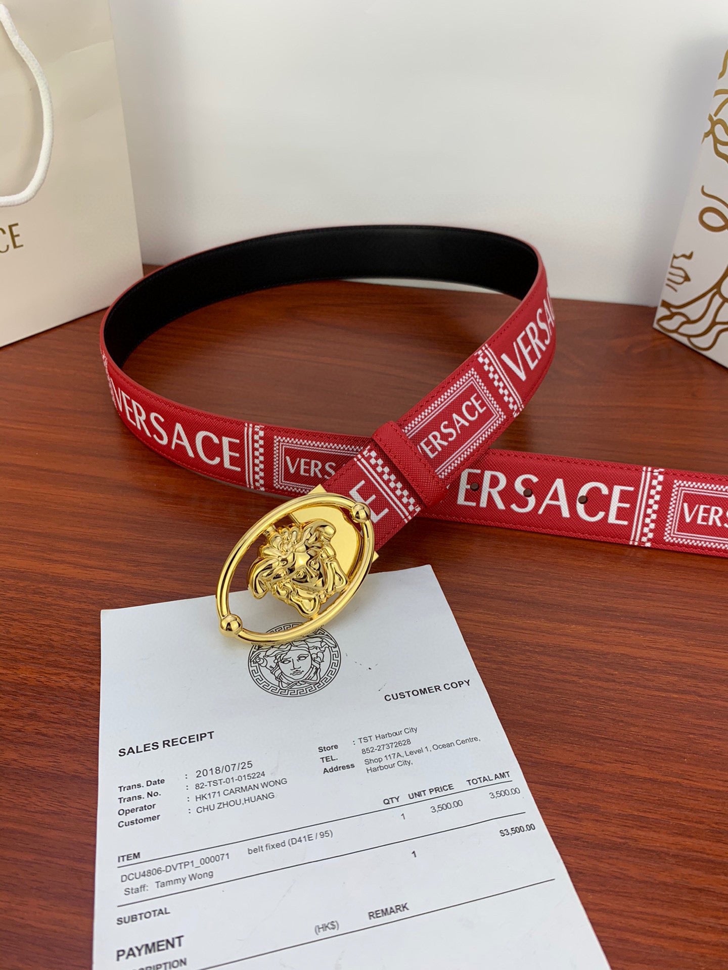 Versace belt loop with gold Medusa buckle on red logo strap placed on sales receipt paper.