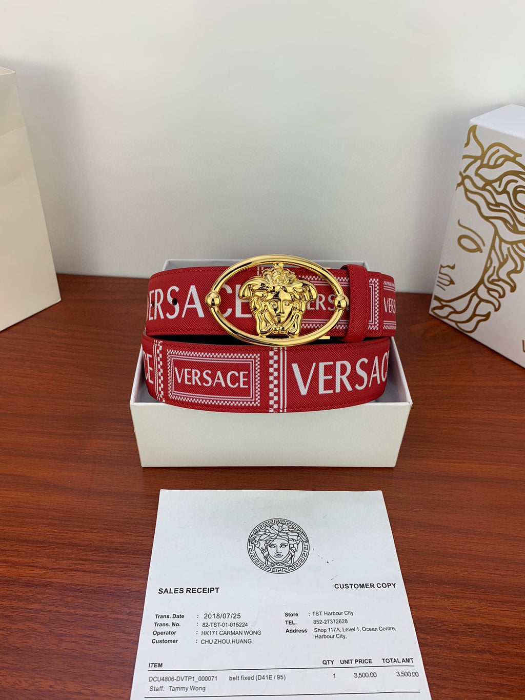 Versace belt coiled in box: red strap with VERSACE logo blocks and gold oval Medusa buckle.