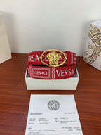 Versace belt coiled in box: red strap with VERSACE logo blocks and gold oval Medusa buckle.