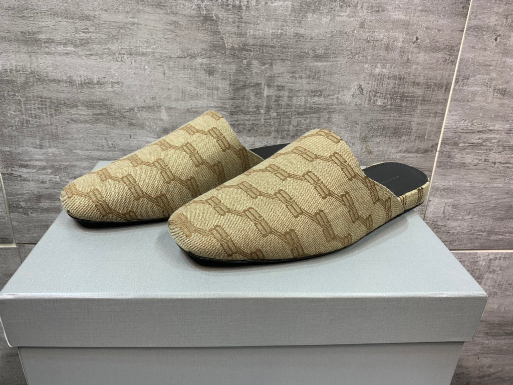 Beige patterned slide sandals with black footbeds, side view on white box