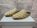 Beige patterned slide sandals with black footbeds, side view on white box